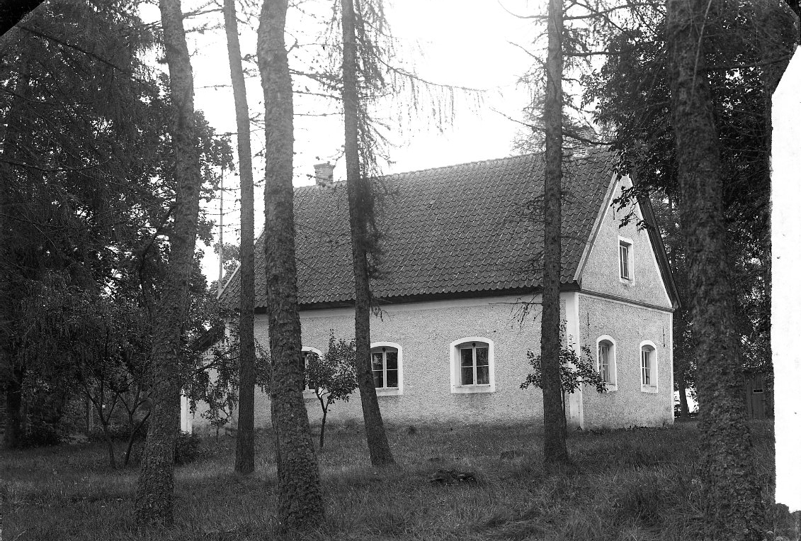 En putsad byggnad bland höga träd. Tingshuset på Visingsö.