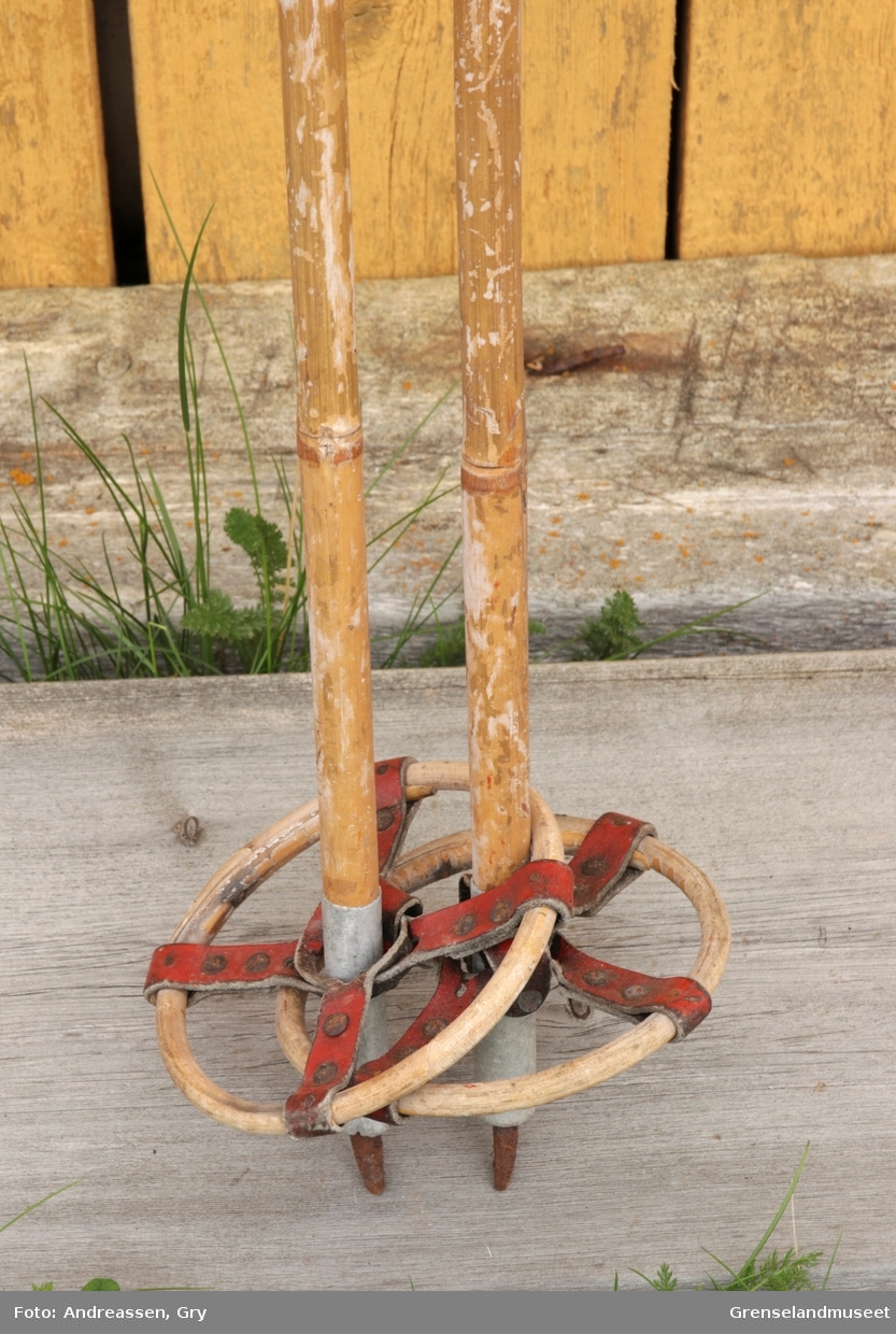 Et par skistaver av bambus med håndtak og stropper i hvitt skinn, pyntet med en tynn bise i rødt skinn. Trinser av bambus og rødt skinn, tupp av lettmetall og jern.
