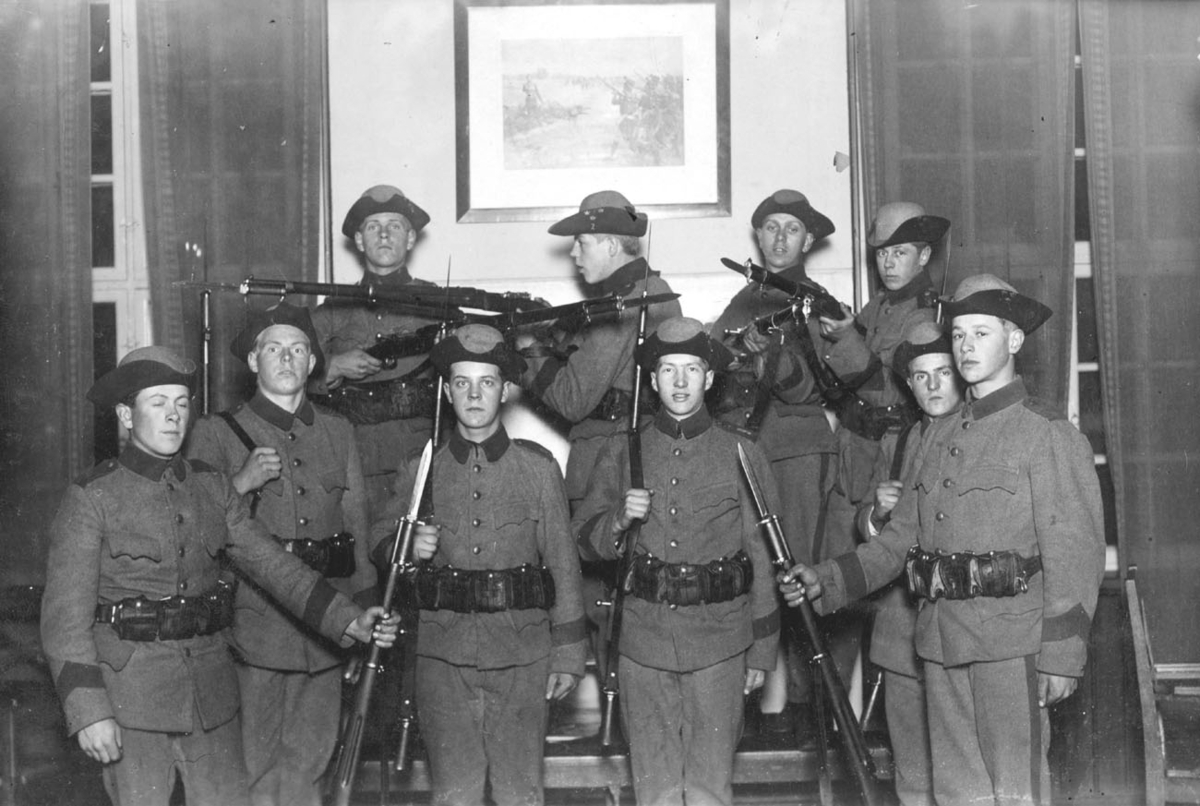 Soldater i uniform m/10 och muskötvapen spexar framför kameran.