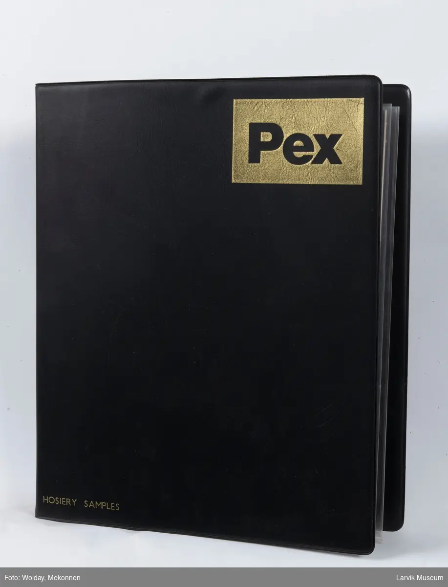 Vareprøver i perm
På forsiden av permen står det: Hosiery samplex  merke:PEX 12 stk. barnesokker pluss noen stoffprøver ligger i en sort plastperm