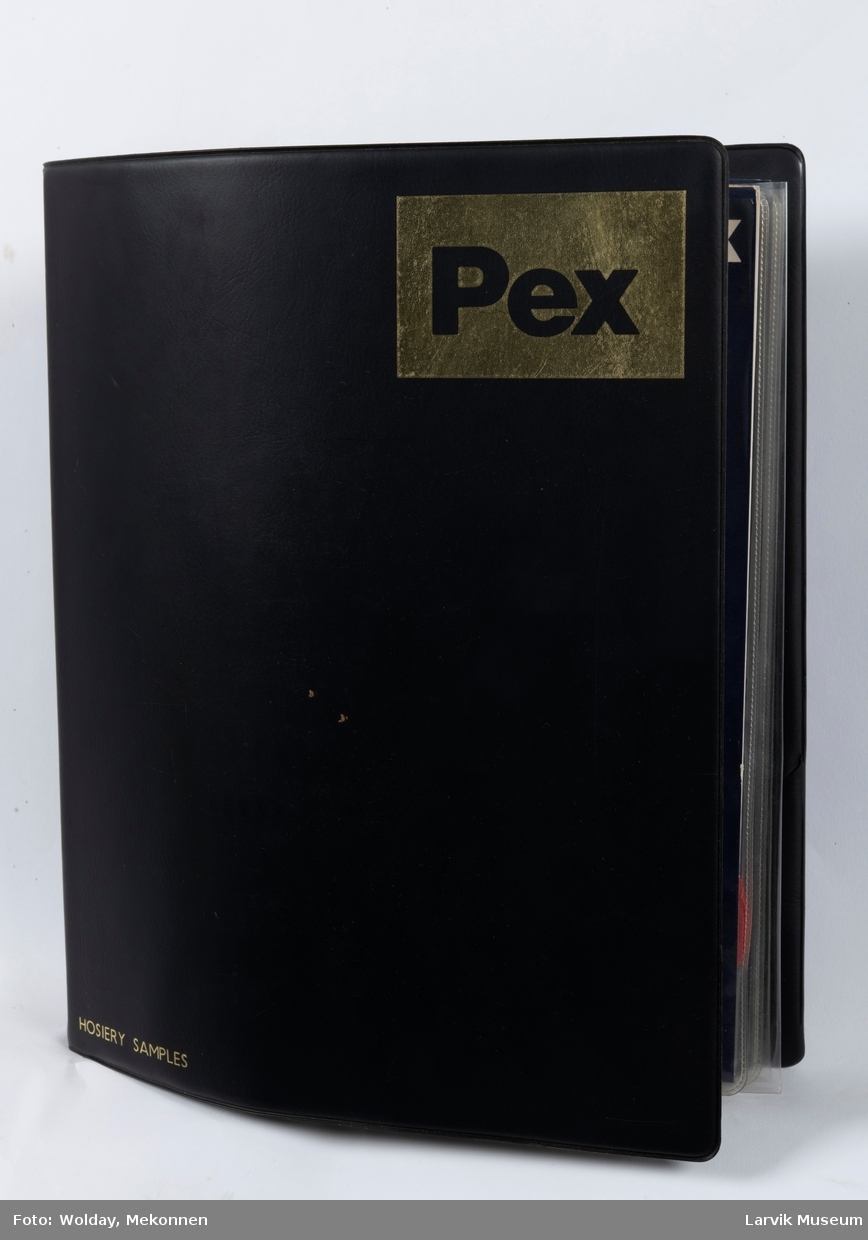 På forsiden av permen står det: Hosiery samplex  merke:PEX 18 stk. barnesokker pluss noen stoffprøver ligger i en sort plastperm