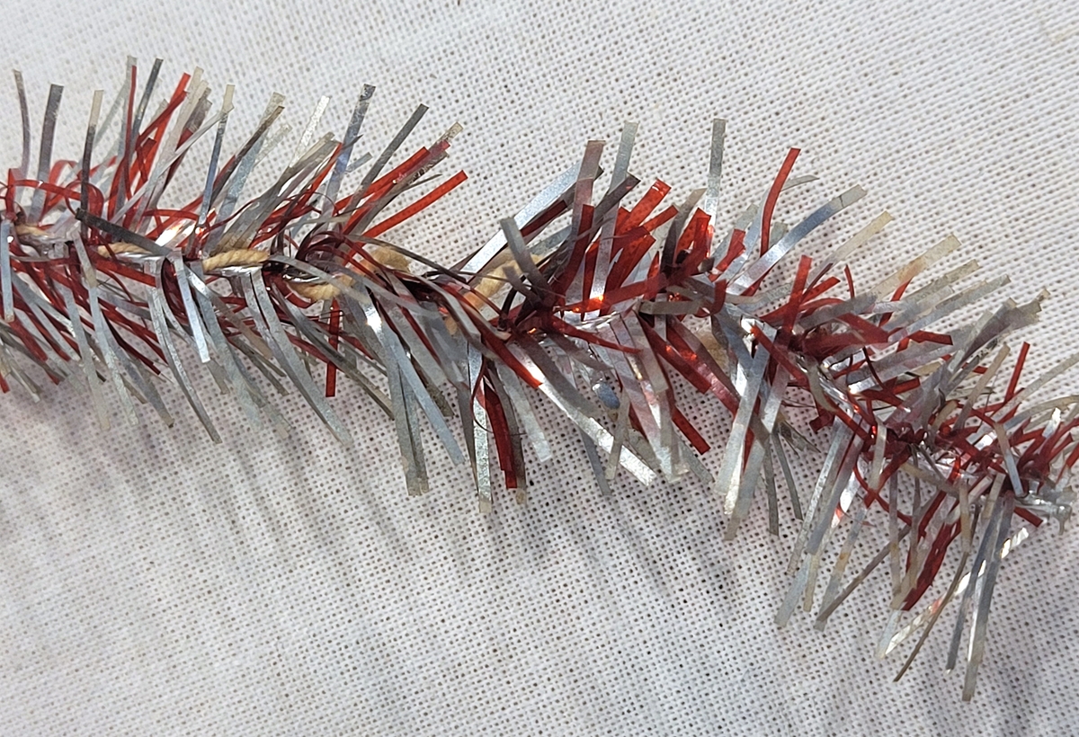Lenkene er av tvunnet bomullshyssing med glittertråder i rødt og sølv stukket inn i hyssingen på tvers.
