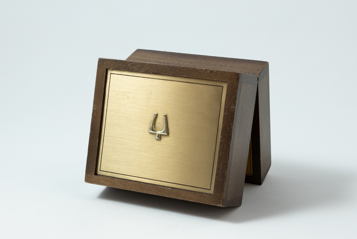 Rektangulær klokkeboks med festet lokk. Inne i boksen er c-formet pute til å ha armbåndsur på.
