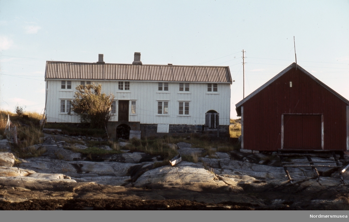 Foto fra et bolighus og naust, muligens i Smøla kommune i Møre og Romsdal. Datering er trolig fra begynnelsen av 1980-tallet. Fra Stein Magne Bach sin private fotosamling. Denne samlingen består av dias fra perioden omkring 1980. Fra Nordmøre museums fotosamlinger.