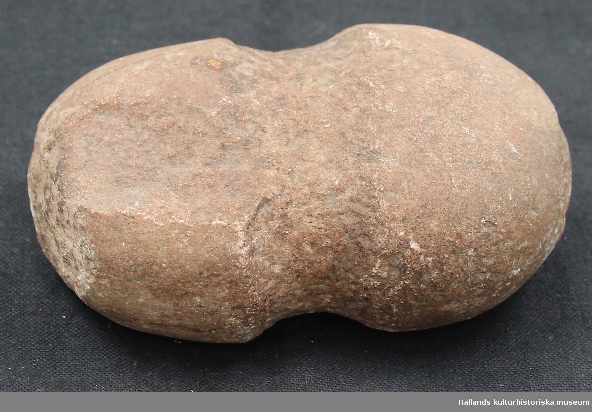 Klubba i sten av neolitisk typ. Knackad och slipad. Bruksslitage på båda huvudena. Äldre skada vid ena huvudet. Ena sidan planslipad.