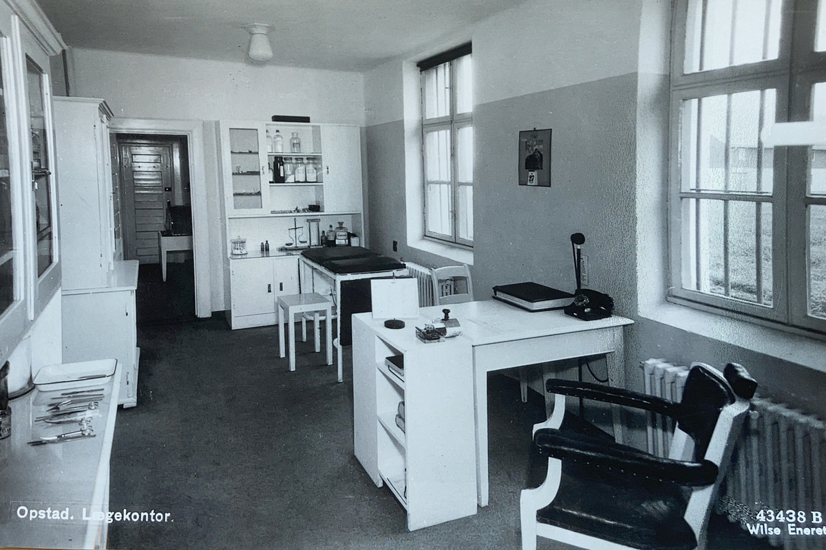 Interiørbilde fra legekontoret Opstad tvangsarbeidshus. Kontoret er innredet med diverse skap for utstyr, undersøkelsesbenk og skrivebord.