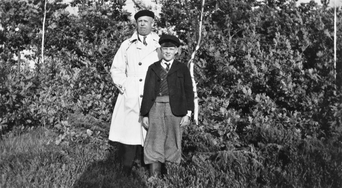 Axel och Bengt Selvén står ute bland lövträd och -buskar. Axel är sannolikt Bengts farfar. På baksidan av fotografiet finns en stor amerikansk stämpel med dateringen 12 november 1933 eller 1938, samt fotofirman Booth Quality Photo CO, Cleveland, Ohio.