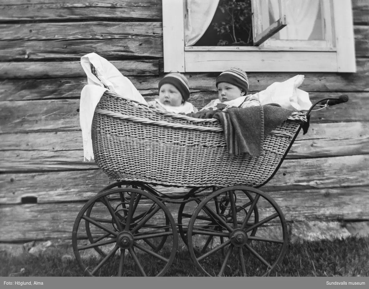 Tvillingsystrarna Anna och Olga Nilsson, Fanbyn, Stöde, sitter i en vacker gammal barnvagn i rotting.