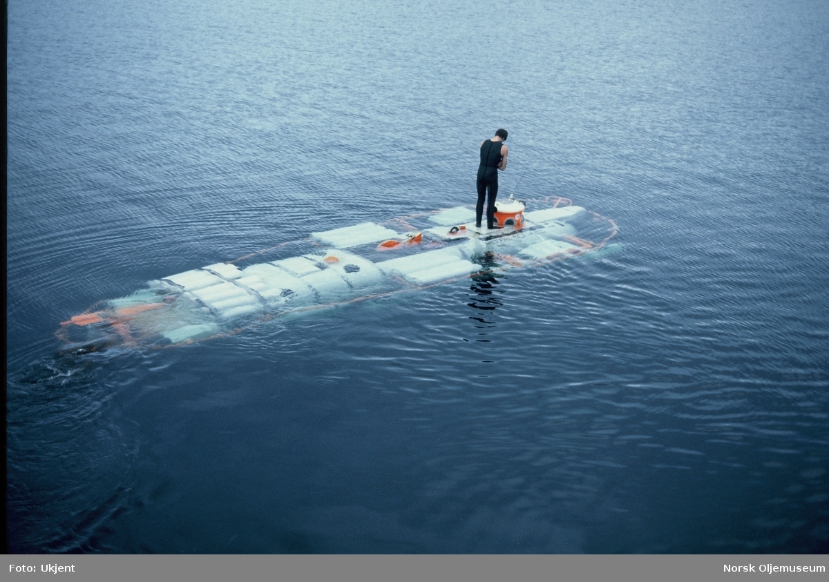 En ubåt løftes fra en lektert og ut i sjøen. En mann i våtdrakt står oppå ubåten under hele løftet.