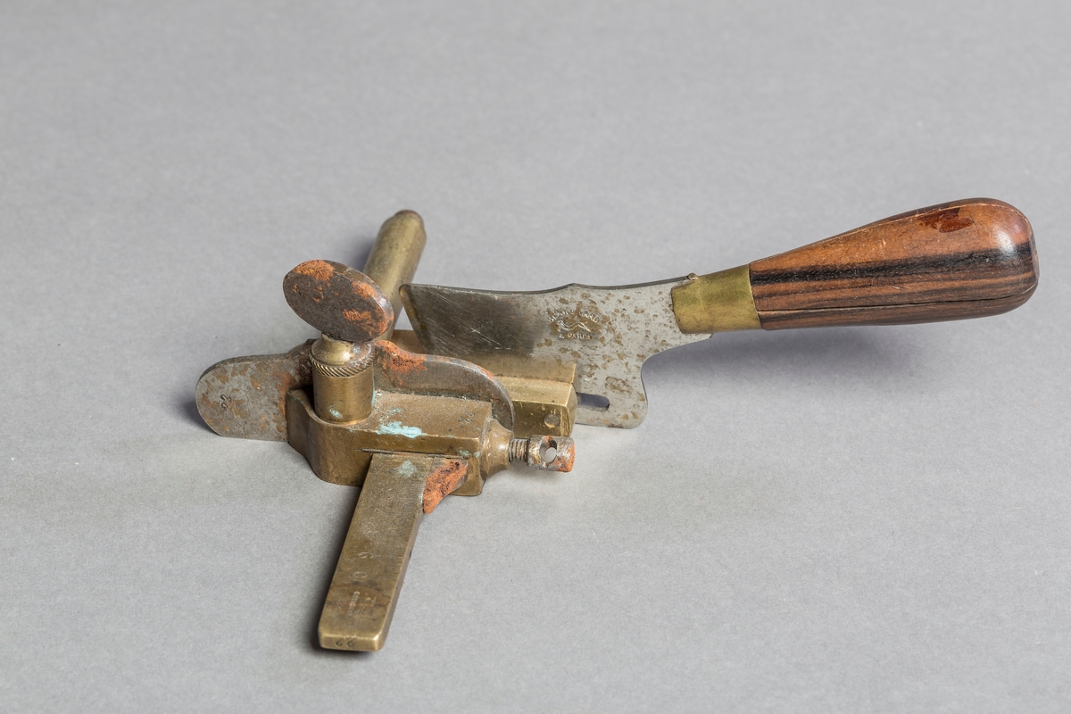 Lærkutter med knivblad i metall og håndtak i tremateriale. Lærkutteren er festet til en skjæreplate med paralellskjærer og linjal opp til 10 cm.