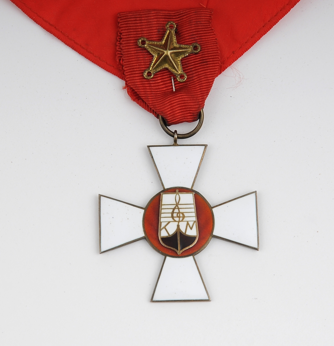 Korsformet medalje som henger i rødt bånd til å ha rundt halsen. Båndet til å ha rundt halsen ser hjemmelaget ut. Nål med femtagget stjerne festet i overgangen fra medaljen til båndet rundt halsen. 