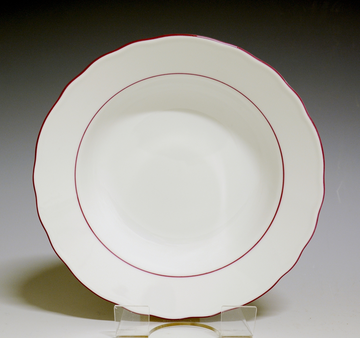 Dyp tallerken av porselen med hvit glasur og rosa kantstriper.
Modell: 1800, Victoria
