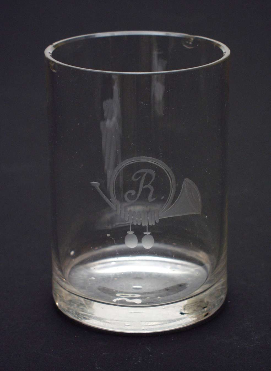 Sylindrisk glass med kraftig bunn. Inngravert et horn med to dusker og bokstaven R.