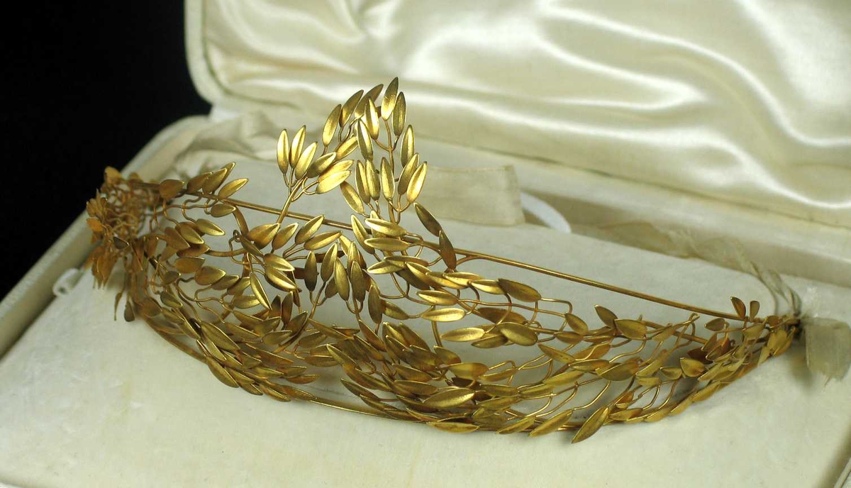 Myrtekrans i gull med hvitt silkebånd bak.
