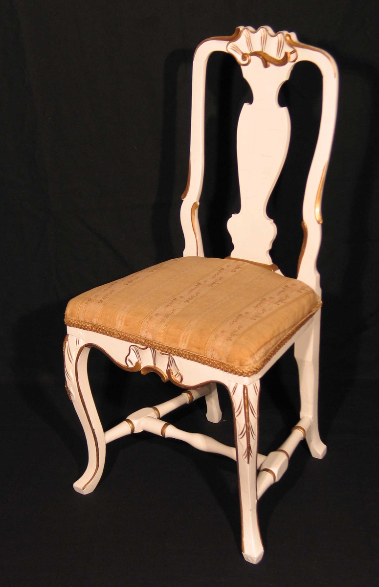 Hvitmalt stol i bjørk med utskåret muslingmønster på toppstykke og sarg. Også utskåret ryggbrett og sprosser. Svungne forben. Bronsemalte detaljer. Setet er trukket om i brokadestoff (skaffet av Dagny.)