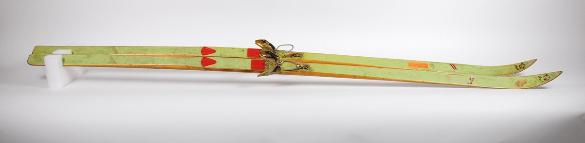 Grønne treski med gullfargede Rottefella-bindinger. Skiene har rød stripedekor på sidene og røde plastkapsler for skoene.