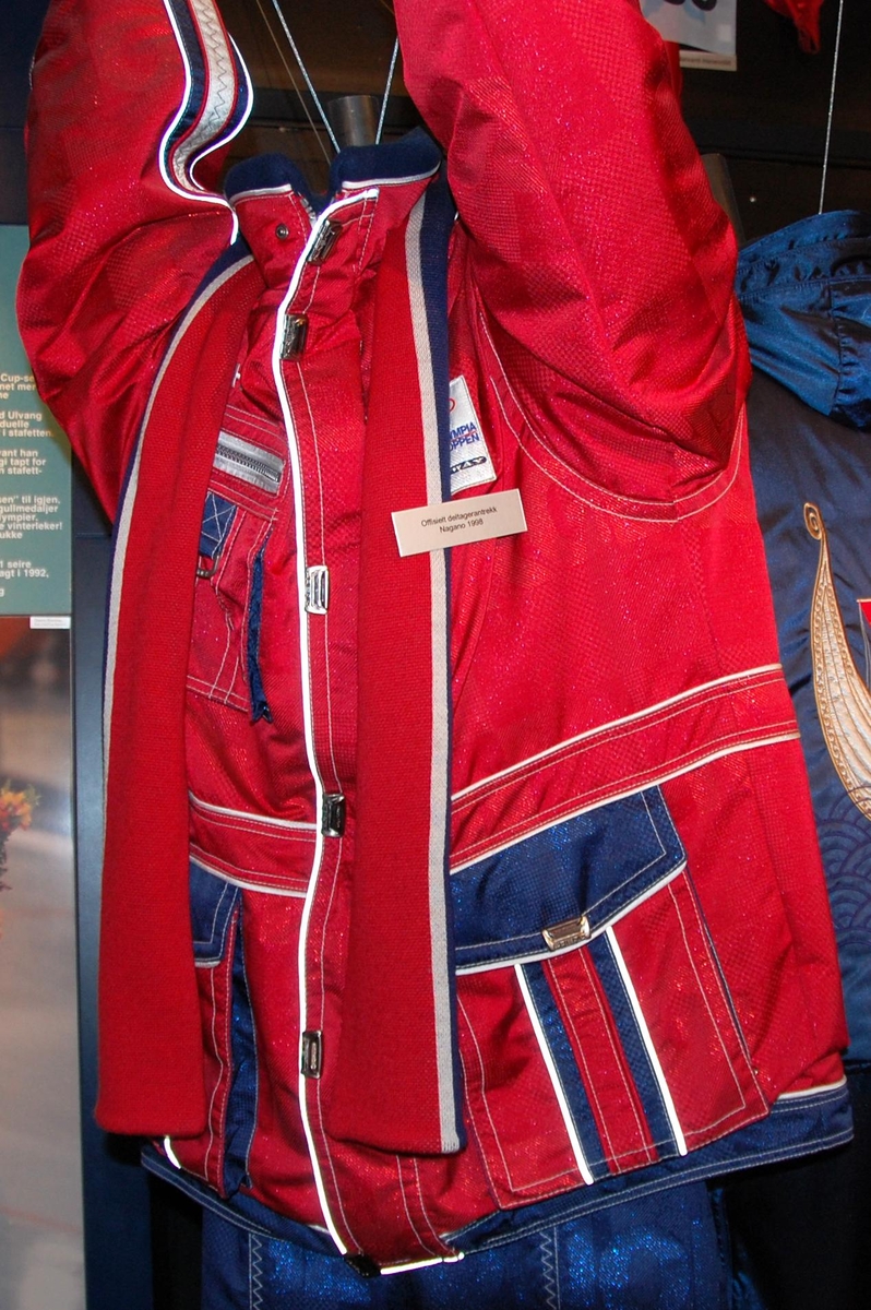 Rød jakke med hvite og blå striper. Jakken har tre lommer. De olympiske ringene i farger brodert på ryggen.