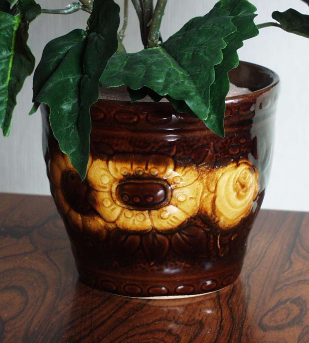 Brun potte i keramikk med blomstermotiv i relieff.