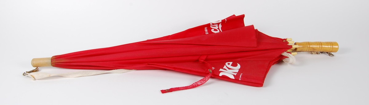 Rød paraply av nykonstoff og trestang inni. Paraplyen har avtagbar bærestropp av et hvitt vevd bomullsbånd. . Coca Cola-reklame i hvitt trykt på paraplyen. Hvert motiv er trykt to ganger.