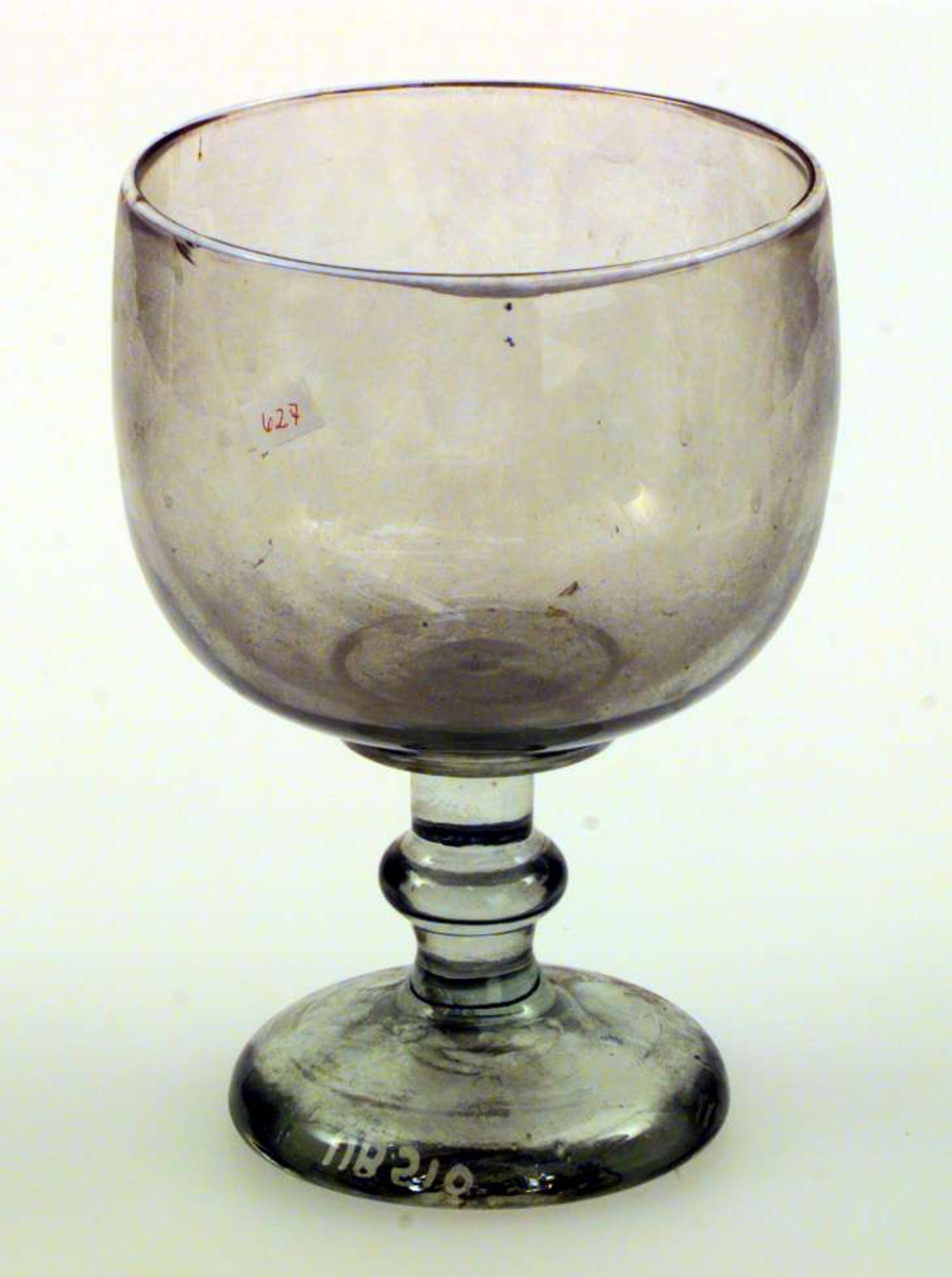 Pokalen er av glass. Den har form som et stort stettbeger. Den er ikke dekorert. Den har hvit munningsrand.