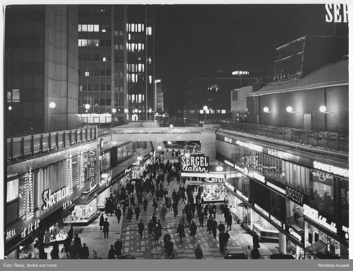 Stockholm. Julmarknad i Hötorgscity. Många människor rör sig mellan butikerna på Sergelgatan. Till vänster i bild syns Hötorgsskraporna.