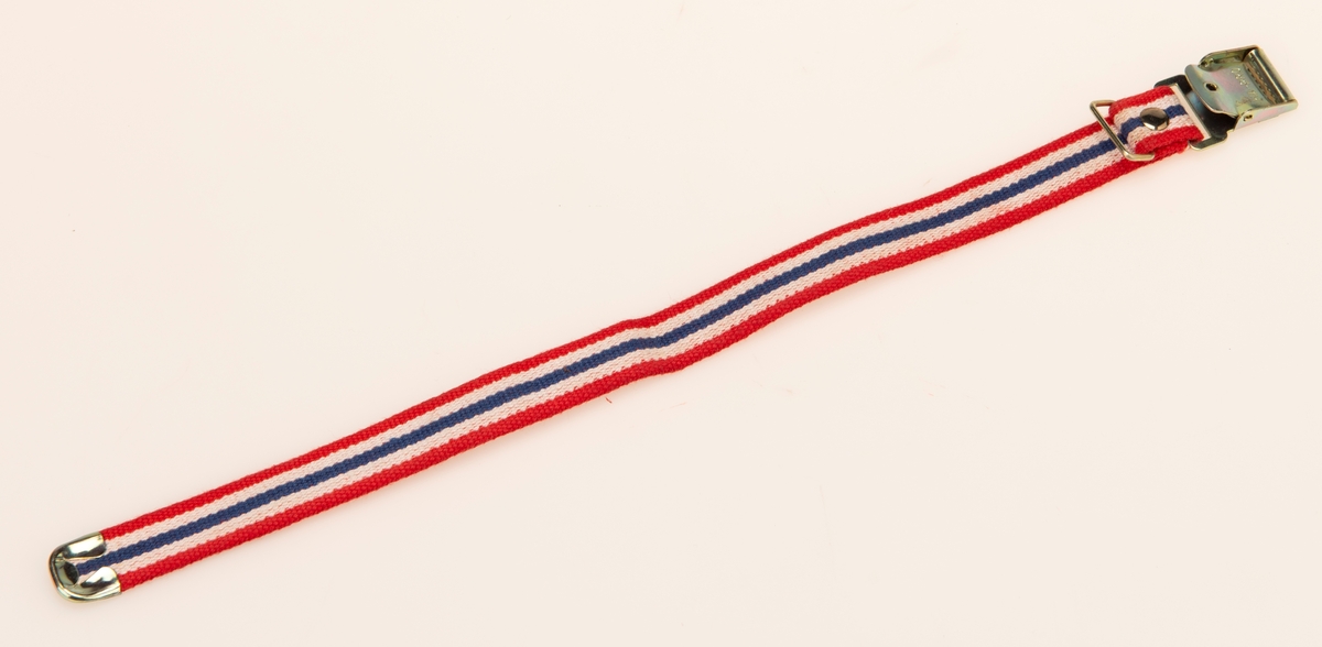 Bomullsbånd vevd i rødt, hvitt og blått. Metallspenne og beslag.