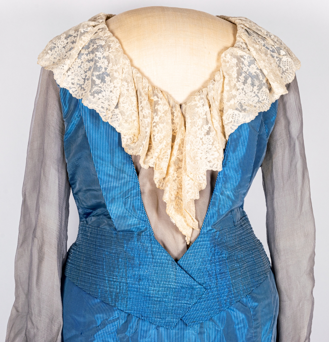 Blå sidenklänning med spetskrage och tyllärmar. Klädda blyvikter monterade för att ge klänningen rätt fall.