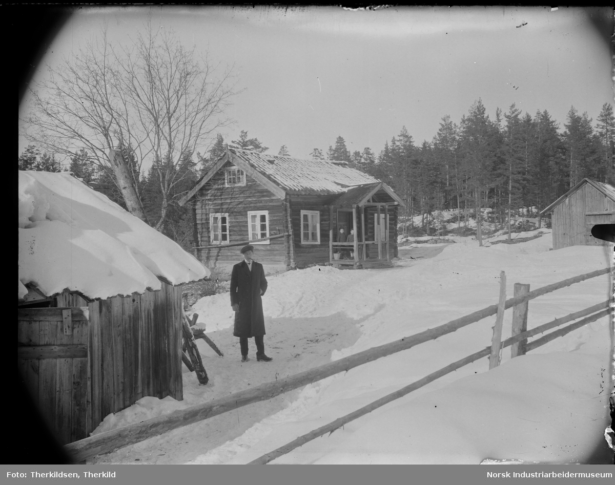 Mann stående foran gårdstun med tre bygninger på Upp-Kåsa (Lien-Kåsa). To gutter stående under overbygg ved inngangsdør til bolighus.