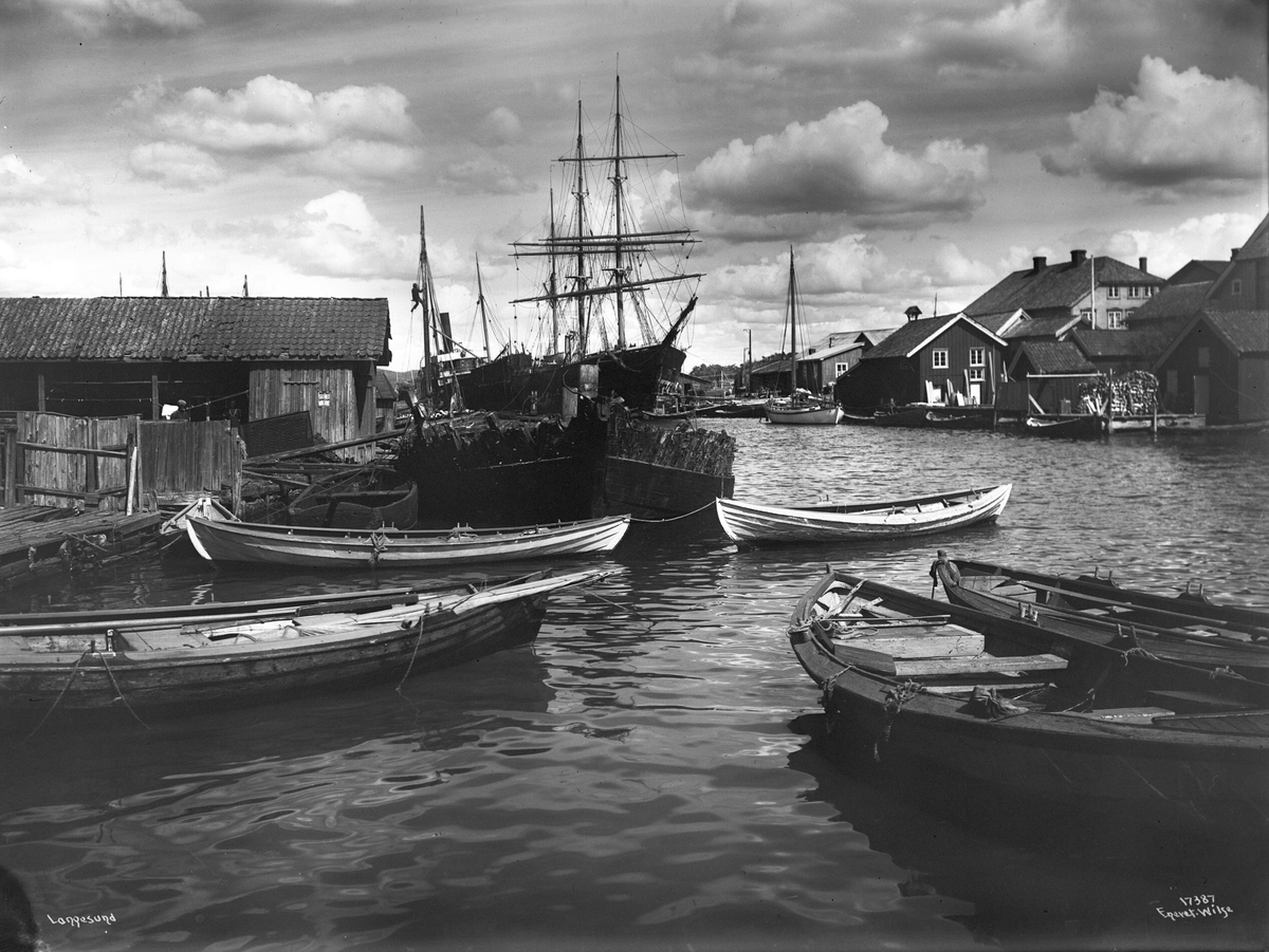 Langesund indre havn med sjøboder, robåter, seilskuter, dampskip og mann som klatrer i mast, 1915.