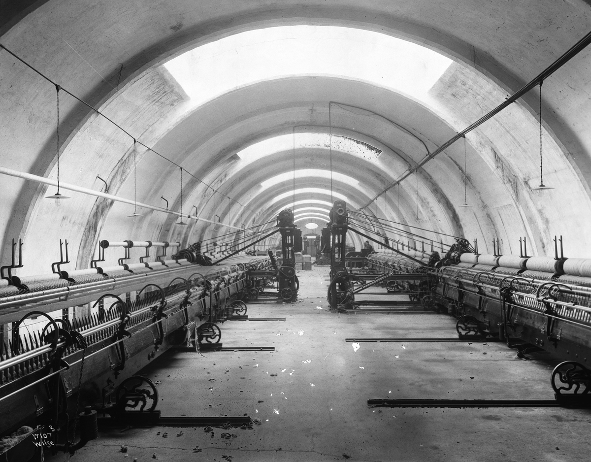 Mange vevmaskiner står i to rader i en hall, Heggdal Ullvarefabrikk. Fotografert 1923.