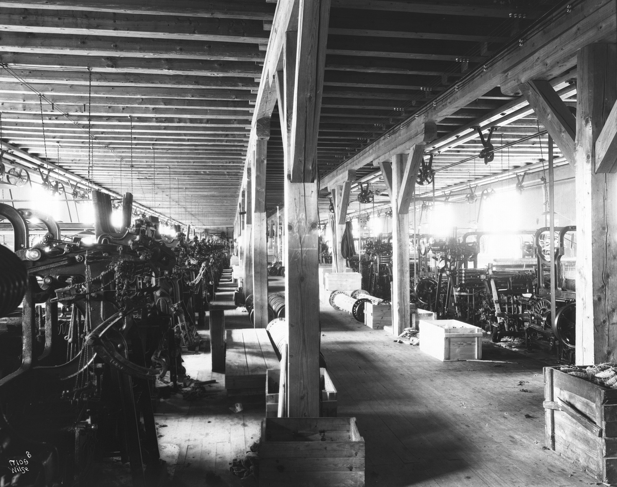 Mange vevemaskiner står i to rader i en hall, Heggdal Ullvarefabrikk. Fotografert 1923.