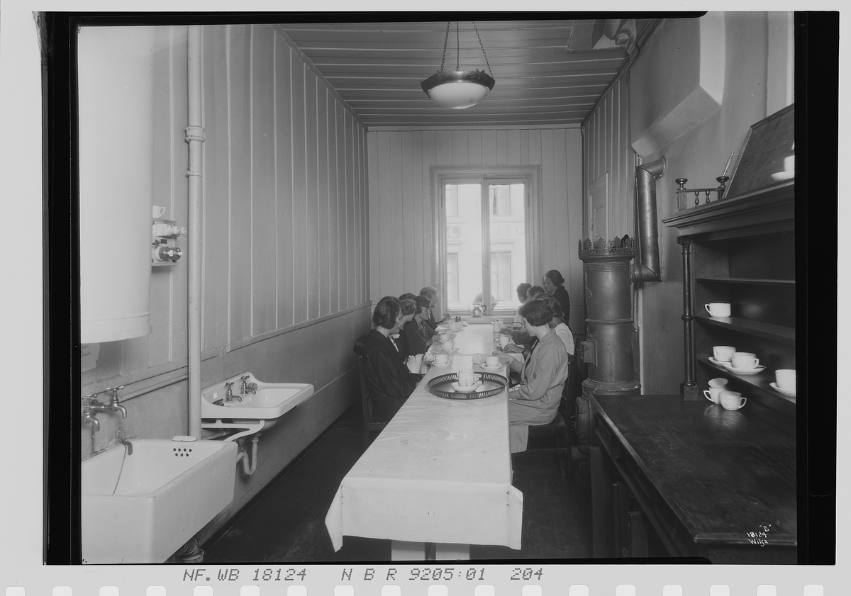 Kvinner sitter langs et spisebord, Vinmonopolet. Fotografert 1924.