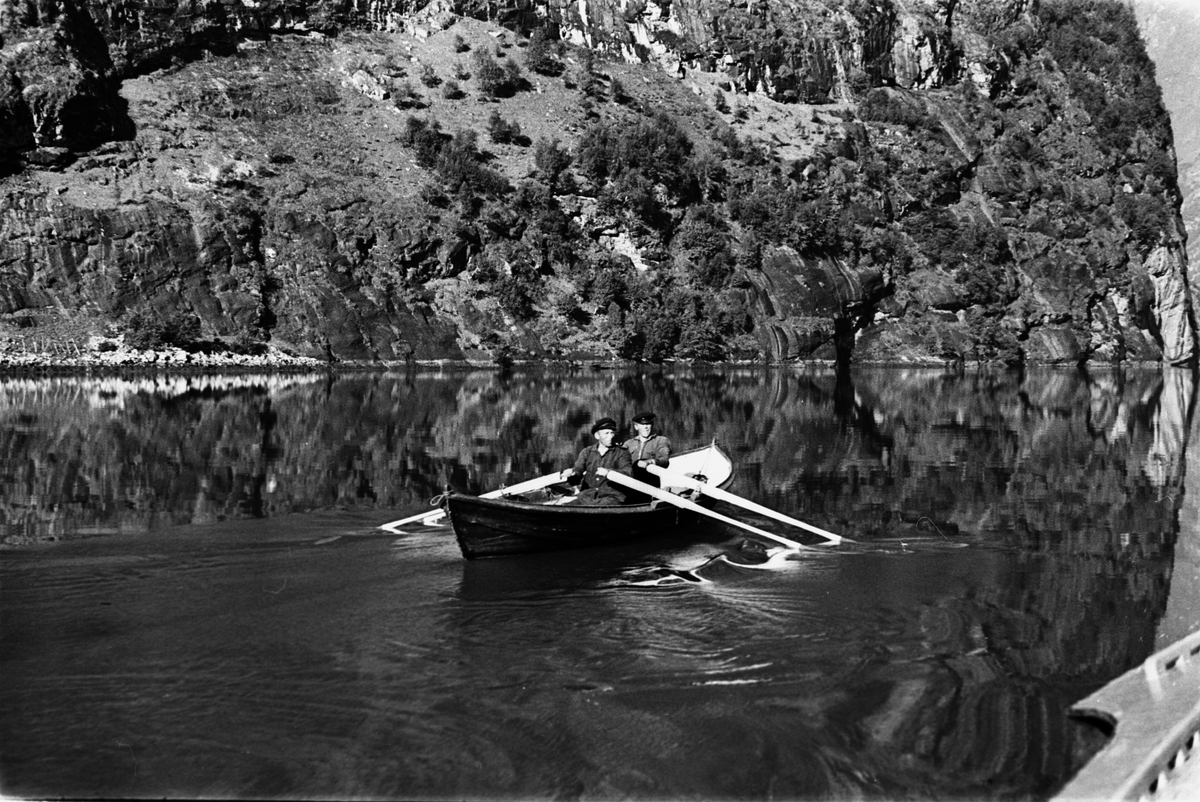 To mann ror og får fart på båten, fjellet ruver i bakgrunnen.