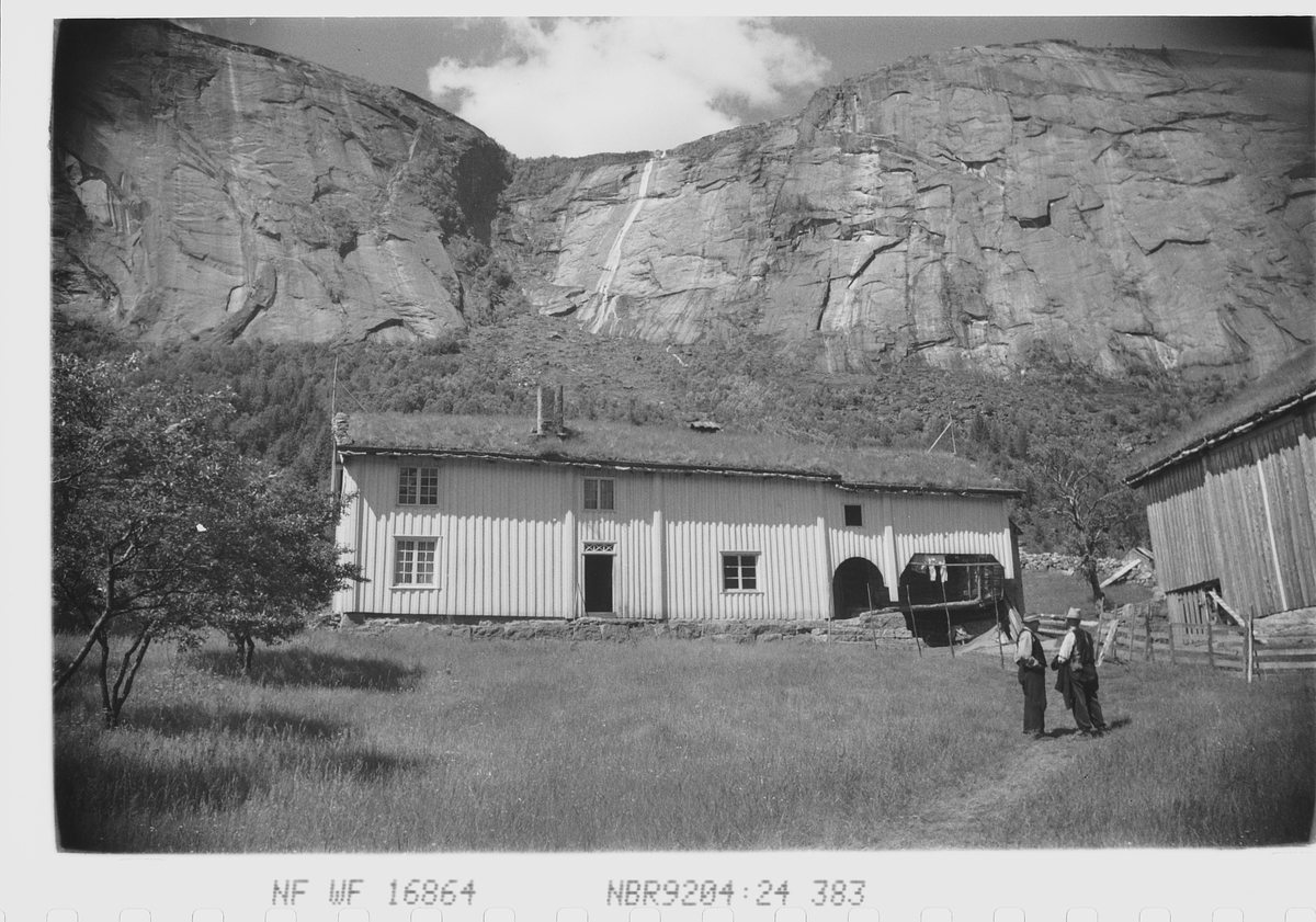 Gårdsbruk i Setesdal, høye fjell i bakgrunnen og setervoll foran bygningen.