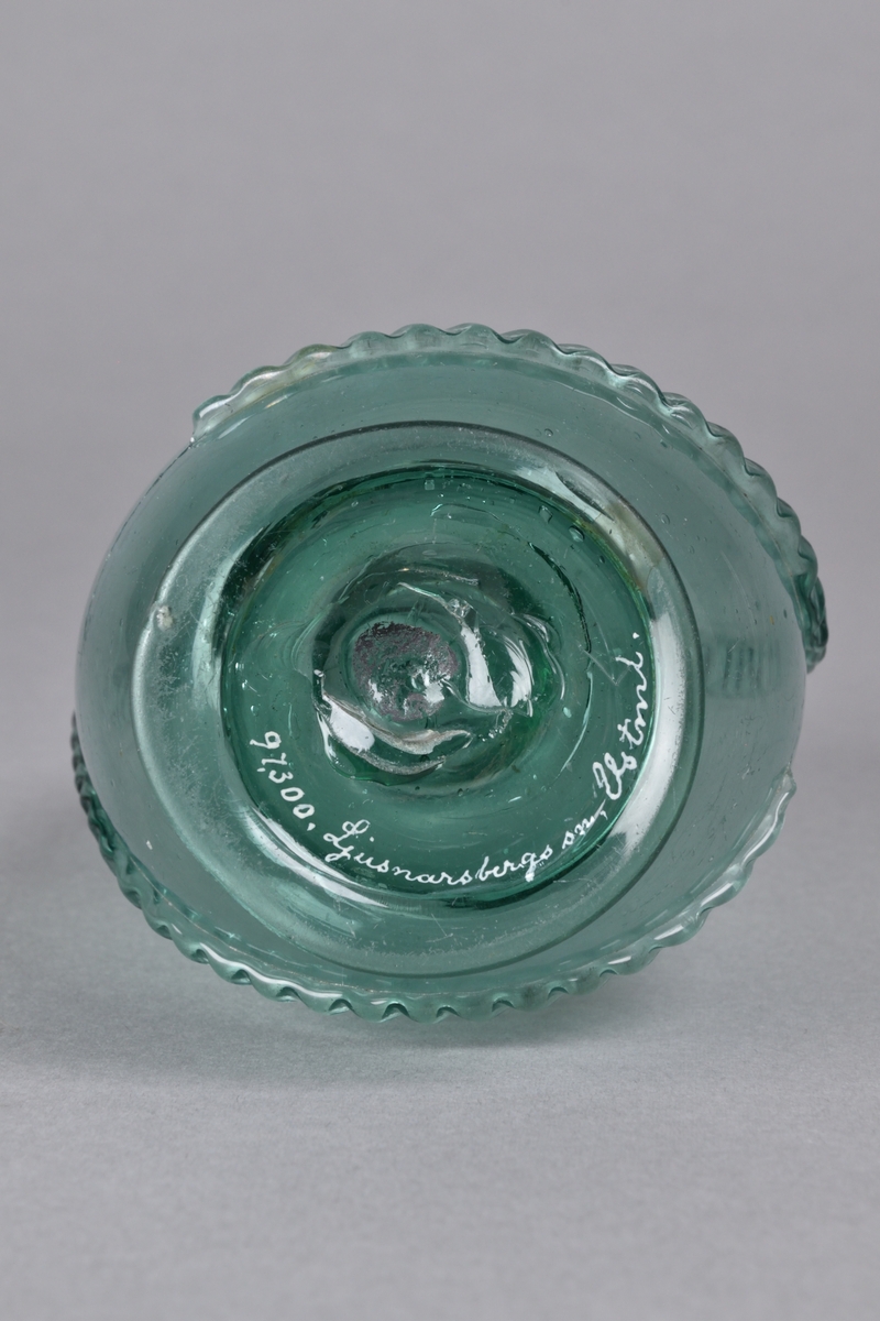 Brännvinsflaska tillverkad i ljusgrönt glas. Bukig nedtill, med ett hoptryckt parti på mitten. Smal och kort flaskhals, med bredare mynning. Dekorerad med en pålagd, räfflad glasremsa. Flaskan står på en låg, rund fot. 