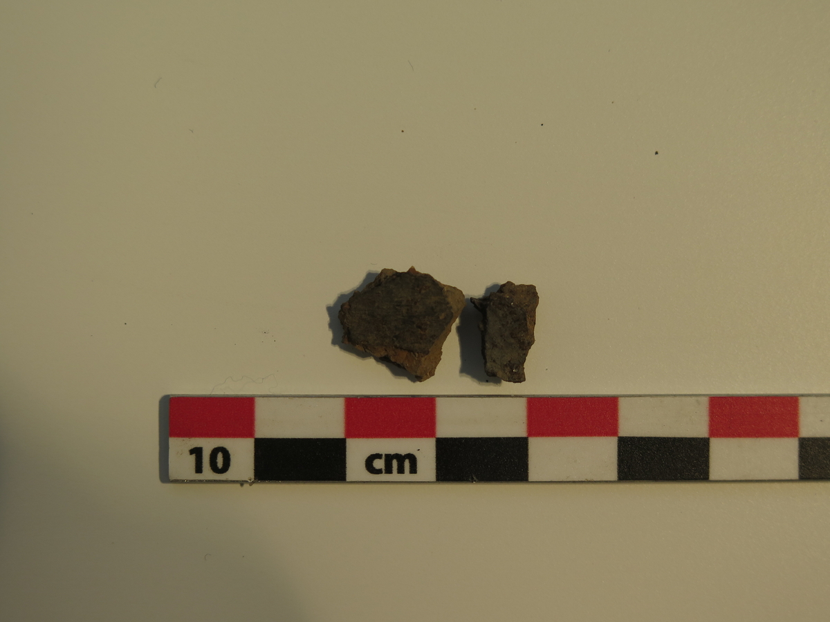 2 fragmenter fra kar av keramikk. Skårene var middels grovt magret, rødbrent på utsiden og mørk brunsort på innsiden. Vekt: 1,2 g. Stl.: 1,3 cm; Stb.: 1,1 cm; Stt.: 0,4 cm.