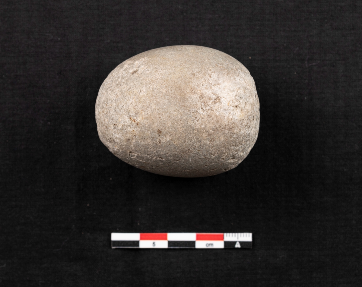 En knakkestein av bergart med halvoval form og glatt overflate. Steinen er godt brukt i begge ender med tydelige knusningsspor.