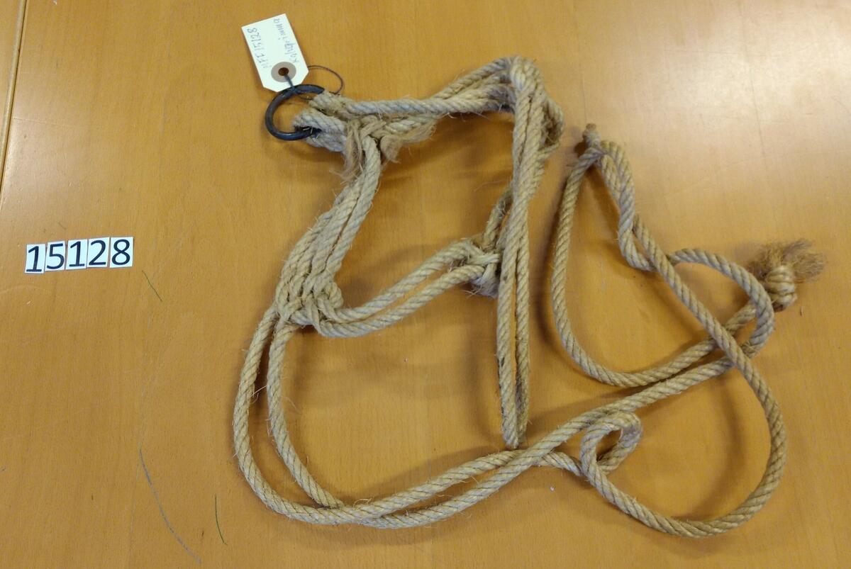 Kalvgrimma av jute. Övre delen består av dubbla rep. Underdelen består av 4-dubbla rep. Stålring under hakan. Två rep att knyta runt nacken. Givare: Harry Sjöström.