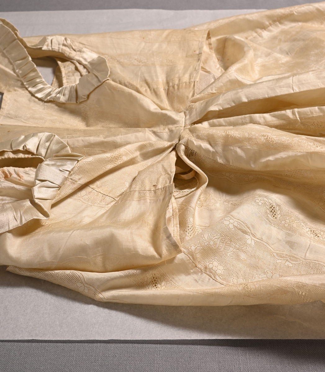 Brudklänning i empirstil från Torpa stenhus, 1815. Naturgul sidenjapon med stansat spetsmönster i form av bredare och smalare bårder med hål- och blommönster. Ärmlöst, kort liv; ärmhålen kantade med rynkad sidensatin. Djup urringning med dragsko av tvinnat silke med tofs i var ände, framstyckena utan knäppning. Innerfoder med dragsko av platt sidenband i ringningen, förövrigt ingen knäppning. Smalt ryggparti, livet endast fastsytt i kjolen mitt bak.

Kjolen samlad i flera veck mitt bak, i övrigt rak med långt släp. Nederkanten kantad runt om med ca 7 cm brett stycke sidensatin med fastsydda veckade rosetter i flortyg.
