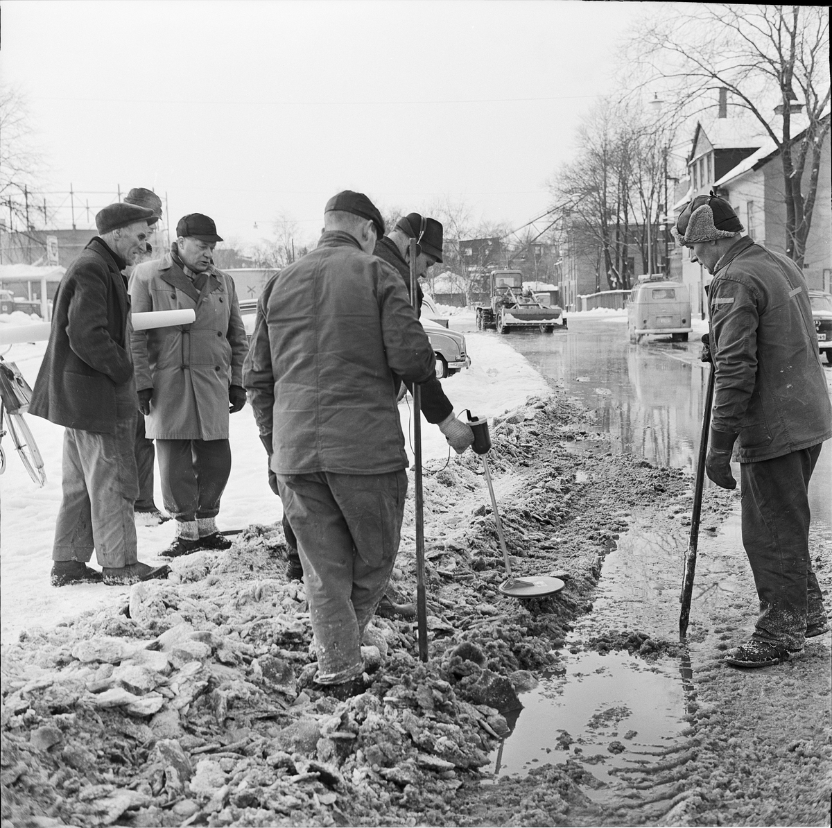 Flera män står vid sidan av Strandbodgatan, några med spett i handen, Uppsala 1966