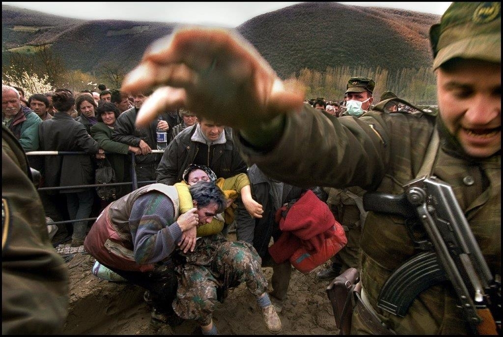 Flyktinger som forsøker å ta seg over grensen fra Kosovo til Makedonia blir stoppet med makt. En mann hjelper en kvinne som har falt.