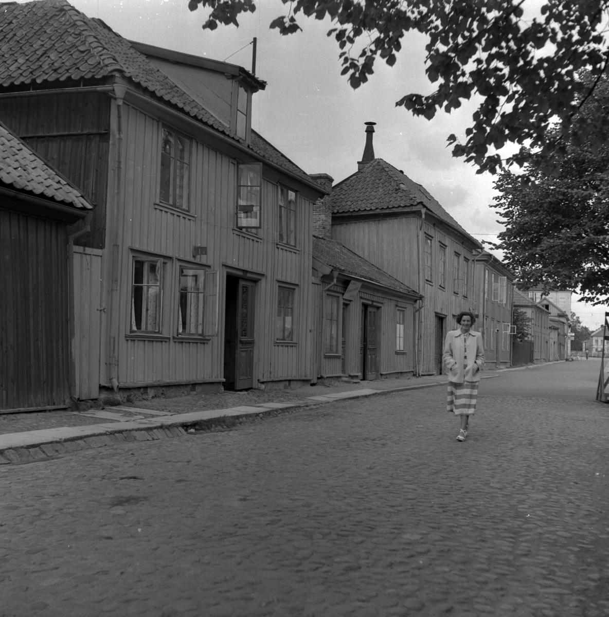 Kerstin Åsén promenerar på kullerstensgata i Jönköping. Längst gatan ligger trähus där fönstren står öppna för vädring.