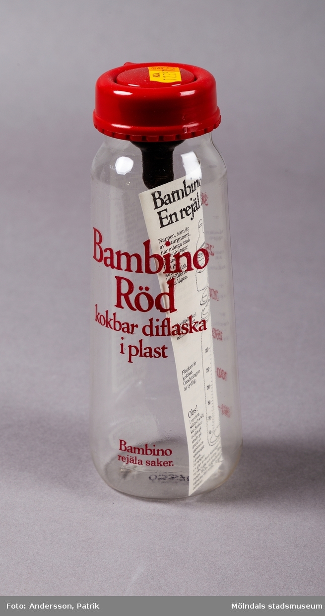 En genomskinlig plastflaska för matning av spädbarn. Flaskan har ett rött lock med napp funktion för matning. På flaskan finns en röd text med varumärket Bambino Röd. Flaskan ser oanvänd ut. Den har en orange extra pris lapp på locket. Den är ursprungligen inköpt på ICA och har kostat 15.60. Inuti flaskan finns en bruksanvisning. Flaskan är från 1981.
Bambino har tillverkat nappflaskor sedan 1950-talet. De marknadsför sig som tillverkare med en smart, funktionell och färgglad design för babytillbehör. Deras kärnvärden är enkelhet, funktion och glädje i vardagen.