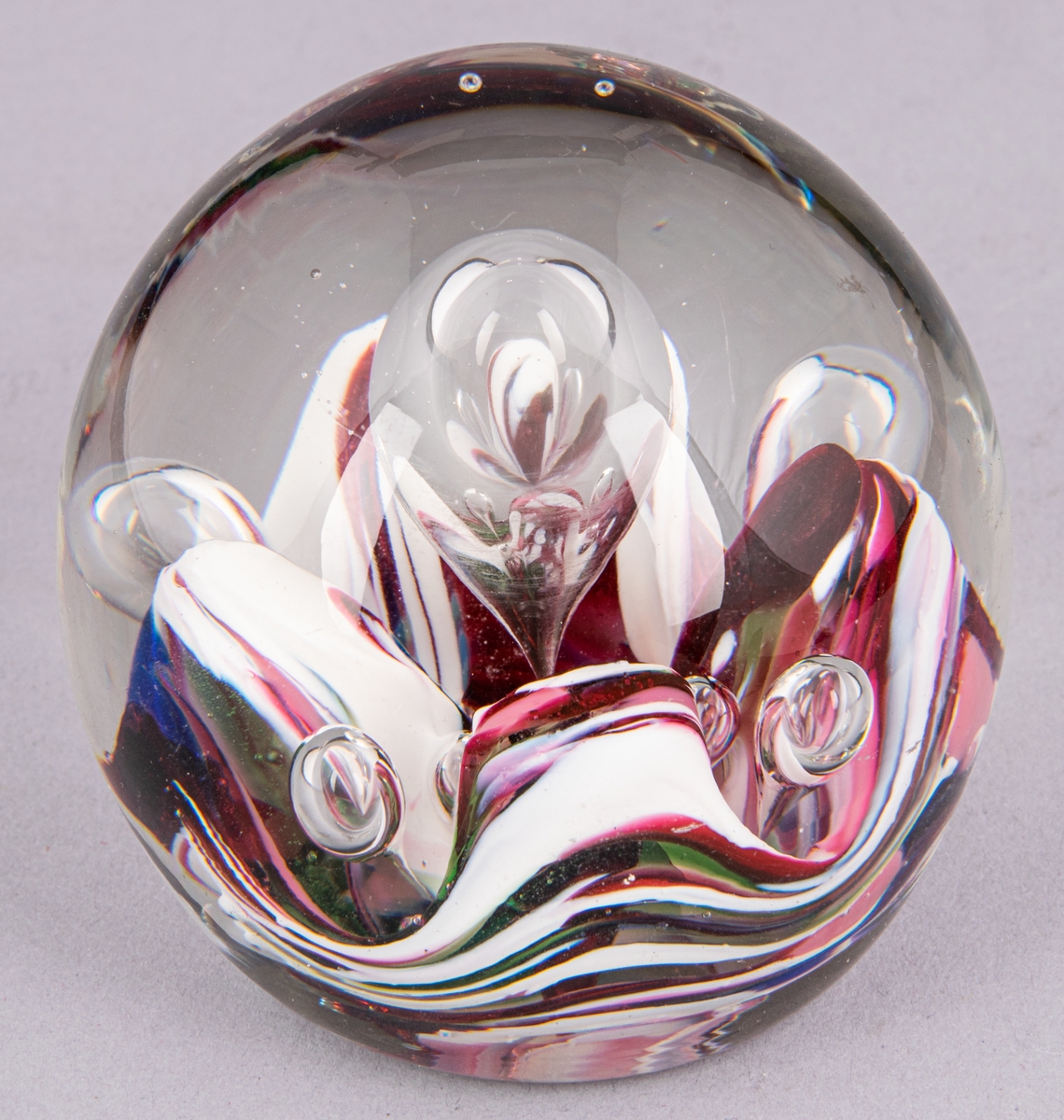 Blåst relativt solid glaskula, genomskinligt glas med vita och cerisea inläggningar.