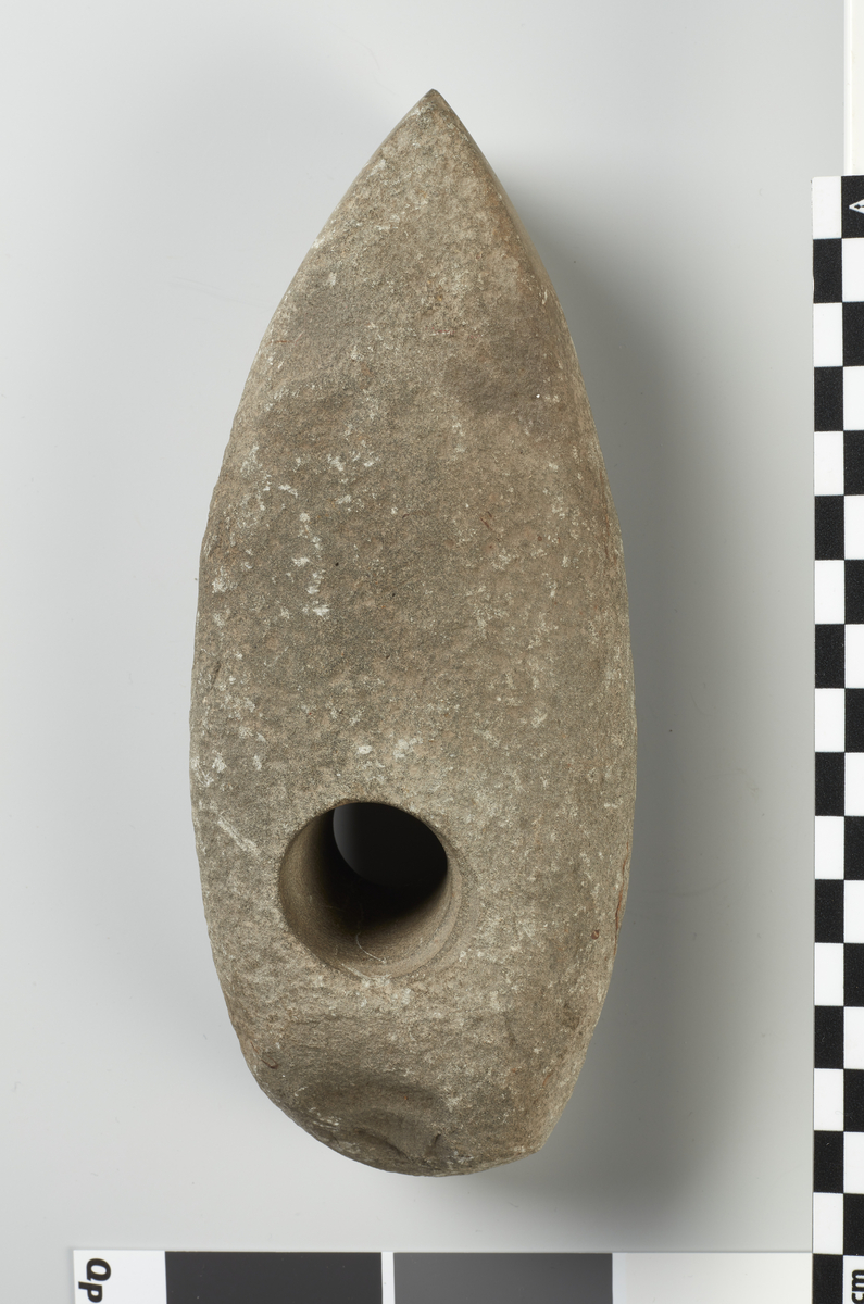 Stenøxe med Skafthul, 18 cm. lang, lig NO. 29, dog mindre hvælvet paa Oversiden, sleben ved Eggen. (12221). F., efter Sigende sammen, paa Gjerdal, ligeledes i Røken.