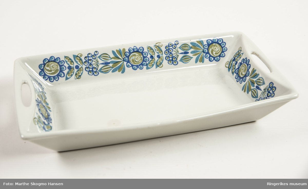 Rektangulært hvitglassert keramikkfat fra Figgjo fajanse med grønn og blå blomsterdekor fra serien TOR VIKING av turi-design, designet i 1973. Dekoren er på fatets innerkanter og kortsidene har ovale gjennomhullet håndtak.