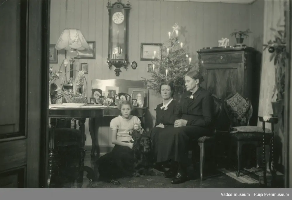 Nyttår i leiligheten til Fru. Simonsen i Vadsø, 1937. Gerd Simonsen sitter på gulvet med hunden ved siden av seg og dukke på fanget. Ved siden av sitter Lilly Simonsen og Emma Simonsen.