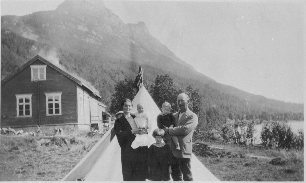 Sofie og Jens Holand med tre døtre foran et spisstelt. Skolebygningen ved Saltvann til venstre.