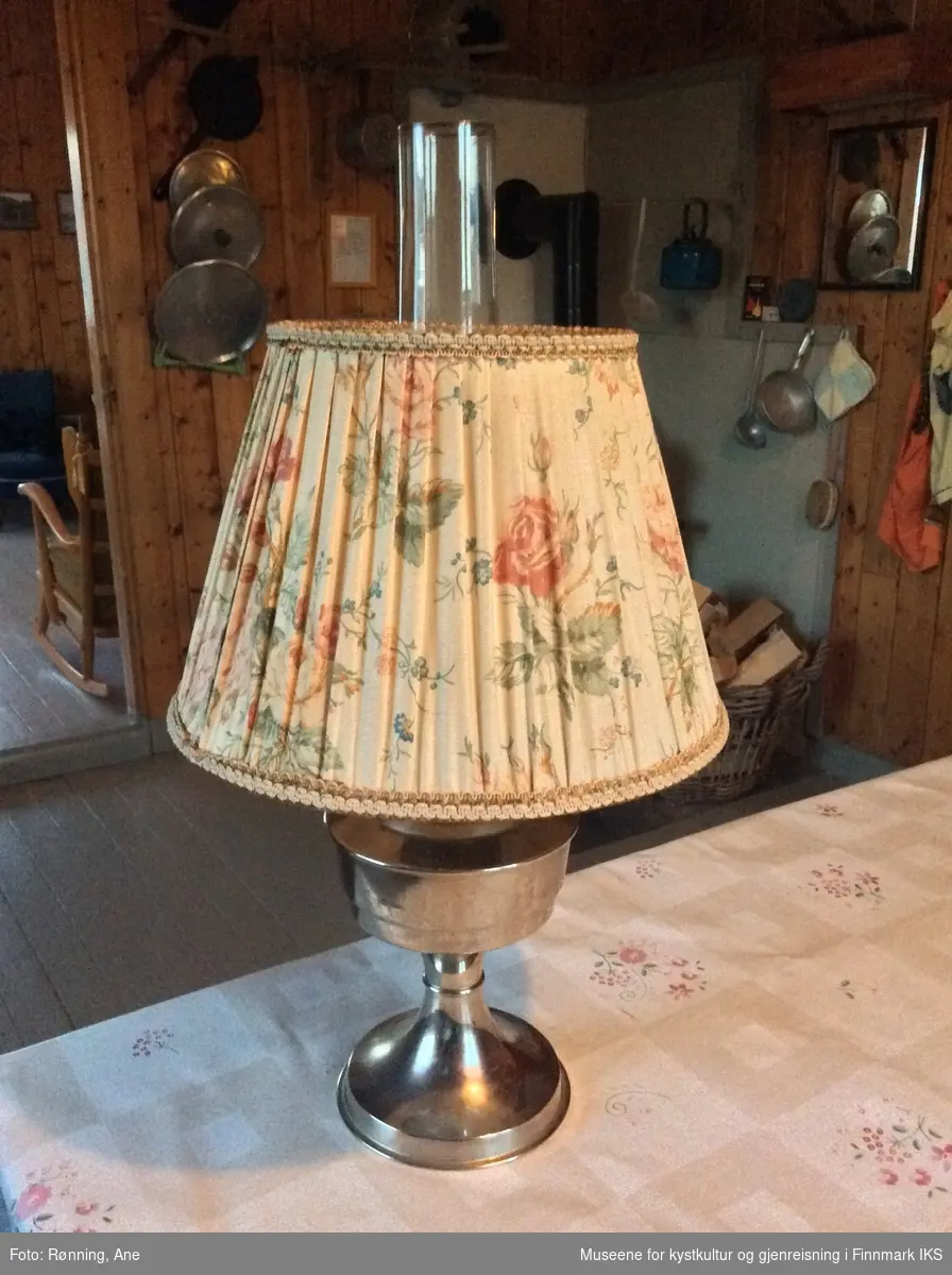 Lampen består av en rund lampefot i metall og har en beholder for flytende brennstoff. Opp på den er det plassert et sylindrisk glassrør som beskytter flammen når det er tent i lampen. Lampeskjermen er av lys, blomstret stoff som har et hull etter en brannskade.