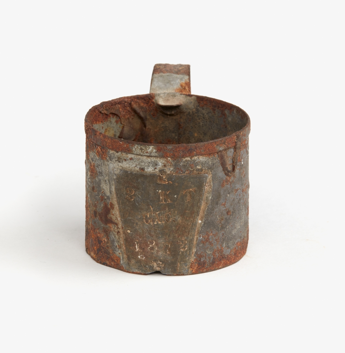 Målkärl av förtennt bleckplåt, cylindriskt med bandformigt handtag, krönt på fastlödd blyplåt "1872", "2 KT" (kubiktum) och "C.A.C." Beckliknande bottensats.
1 tum = 2,47 cm.